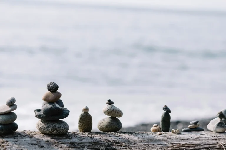 A series of stones balancing on a log in front of the ocean.