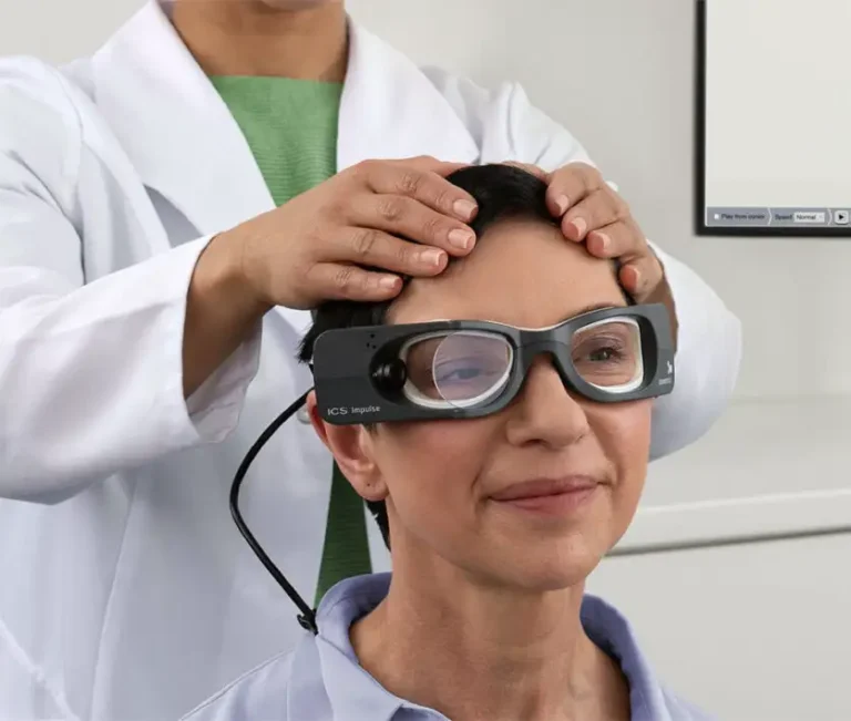 A patient wearing Natus ICS Impulse goggles while a doctor stabilizes her head.